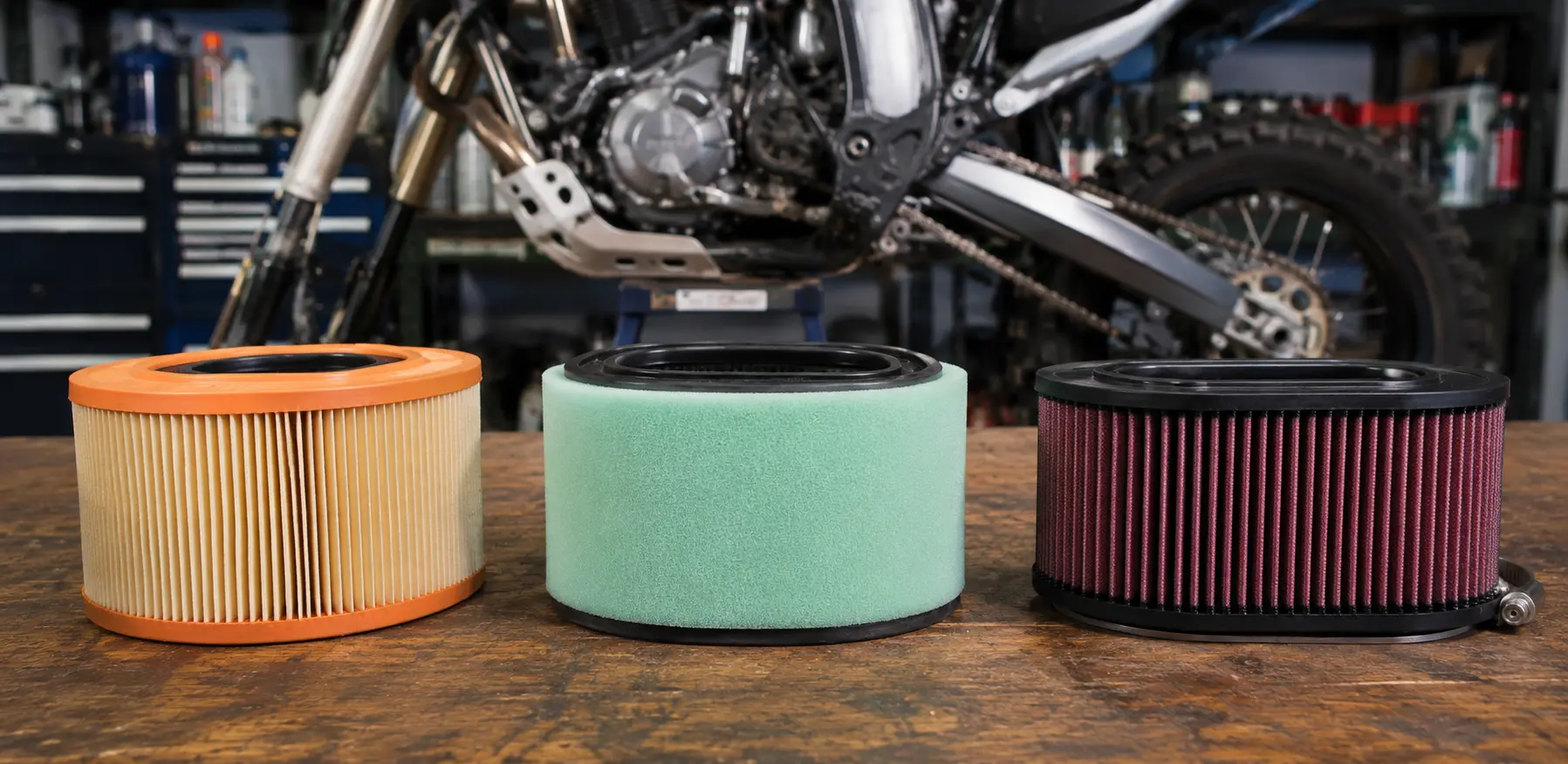 Paper, foam, and cotton gauze motorcycle air filters on a workshop bench.