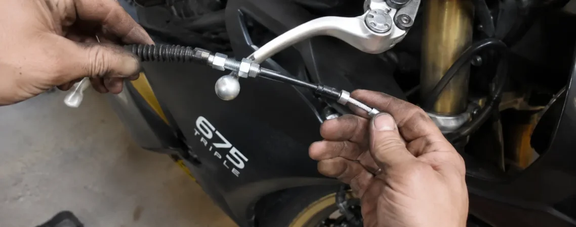 Mechanic replacing a worn brake cable on a Triumph 675 Triple motorcycle in a workshop.