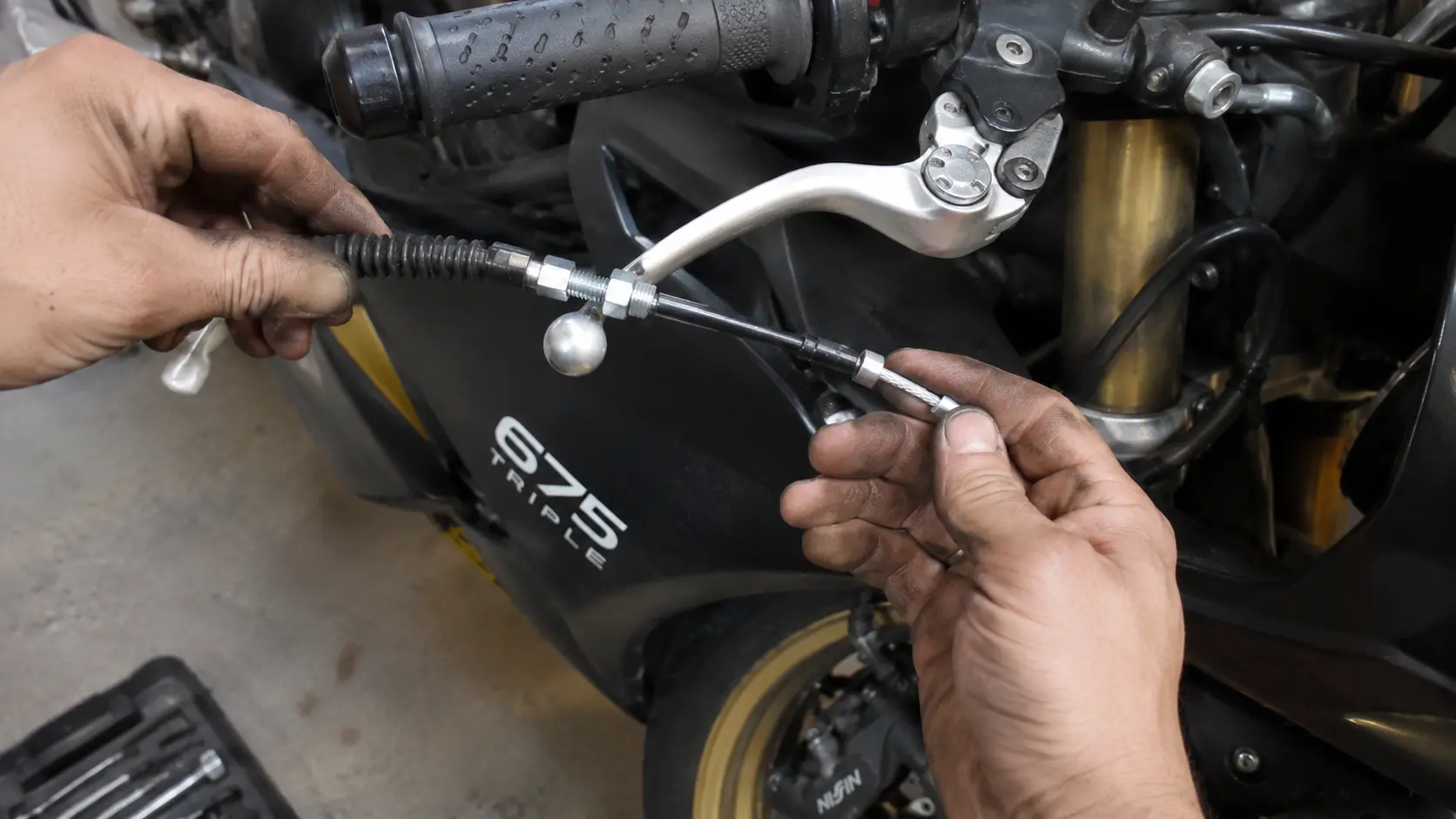 Mechanic replacing a worn brake cable on a Triumph 675 Triple motorcycle in a workshop.